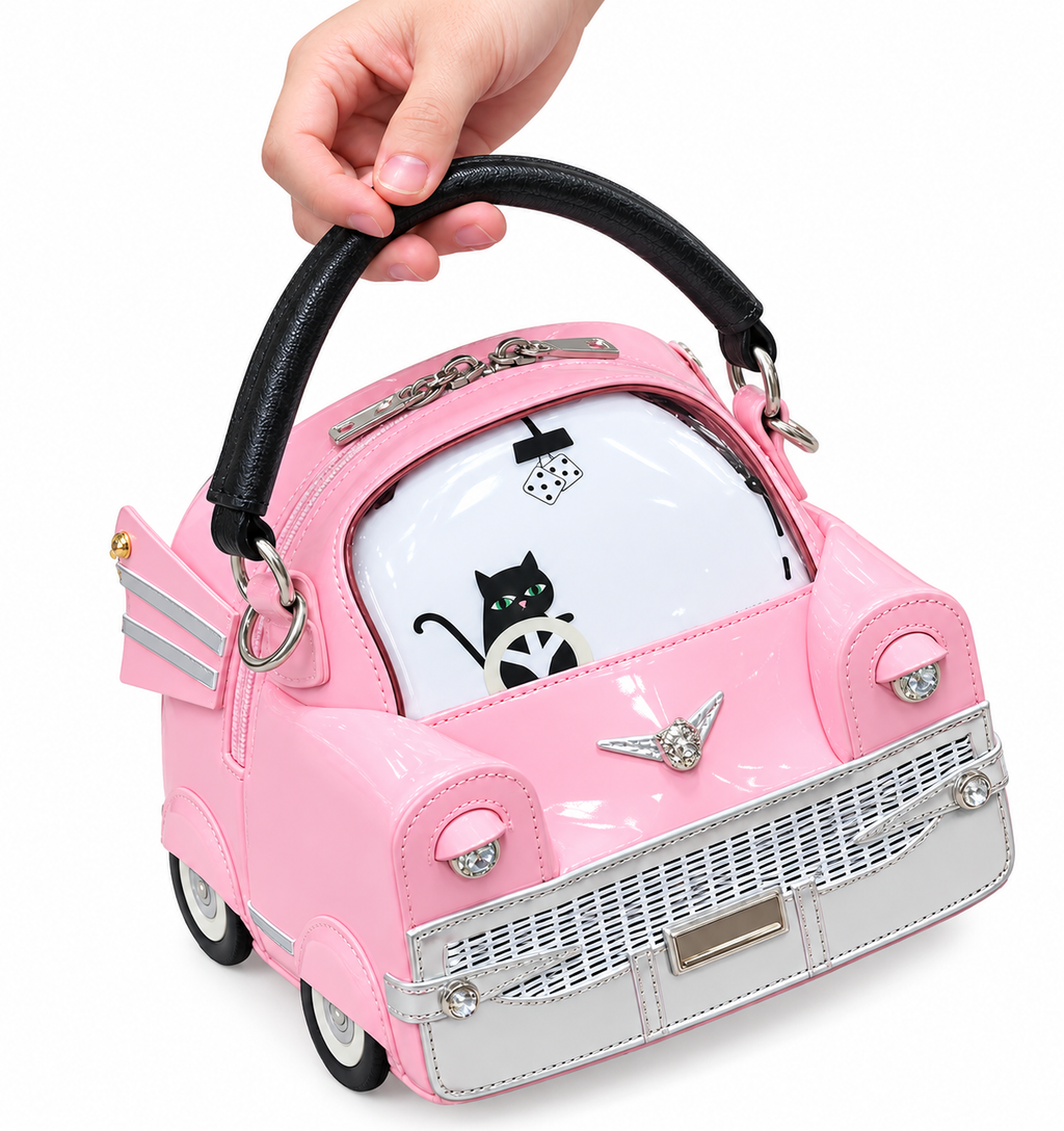 A pink purse shaped like a vintage car, held by a hand. The purse features a glossy pink body, a silver front grille and wheel details, a black handle, and a white windshield with a black cat illustration.