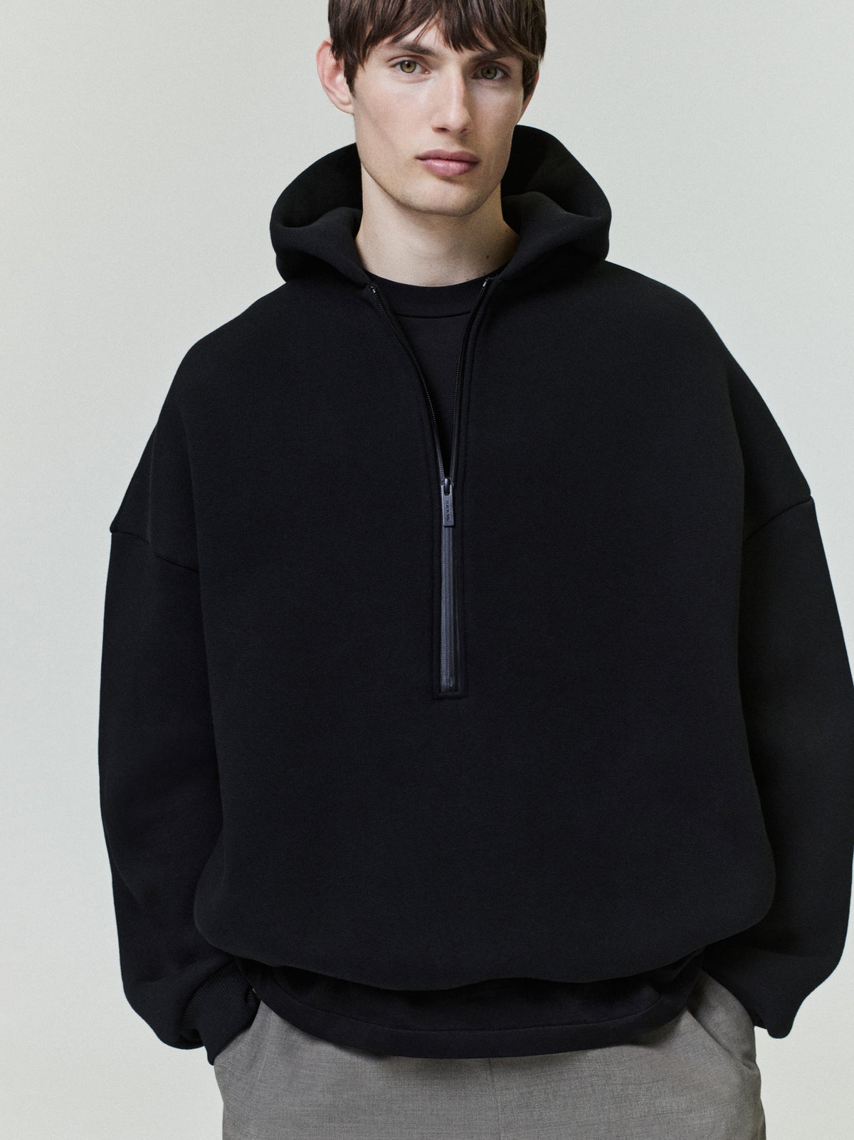 Man wearing a black hoodie with a zipper on a plain background